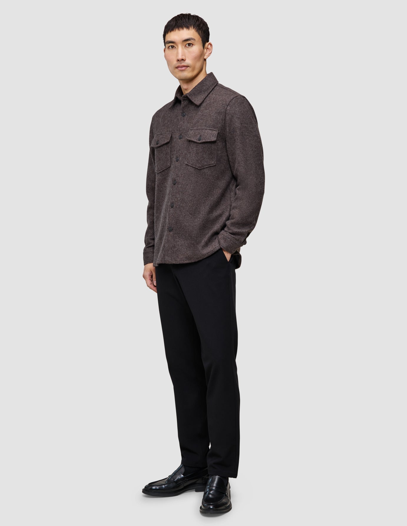 En person kledd i en dobbeltlags ullskjorte i fargen saddle brown, svarte bukser og svarte loafers.
